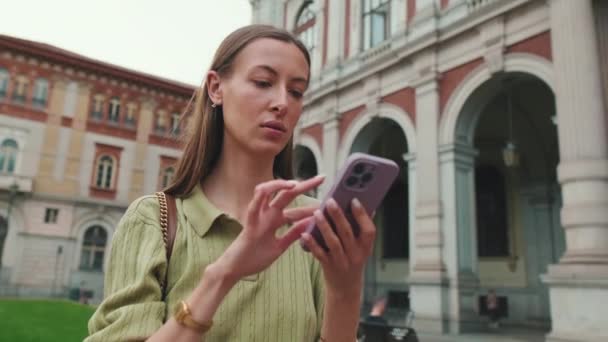 若い女性は古い町の広場に立っている間彼女の携帯電話の地図アプリを使用します — ストック動画