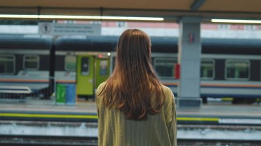 Bir tren istasyonunda bankta oturan genç bir kadın.