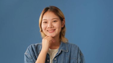 Stüdyoda mavi arka planda izole edilmiş kot gömlek giymiş, gülümseyen genç bir kadın.