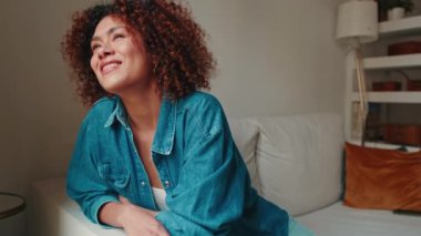 Kanepede dinlenirken pencereden bakan gülümseyen kadın.