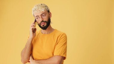 Gözlüklü, sarı tişörtlü, cep telefonuyla konuşan, stüdyoda sarı arka planda izole edilmiş biri.