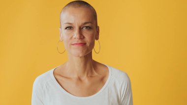 Kılsız genç bir kadın kollarını kavuşturup gülümseyerek kameraya bakıyor. Reklam alanı, Studi 'nin sarı arka planında izole edilmiş.