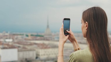 Şehrin gözlem güvertesindeki genç kadın cep telefonuyla fotoğraf ve video çekiyor.