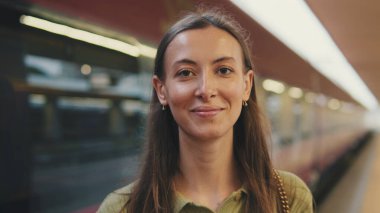 Tren durağındaki kameraya bakan genç bir kadının yakın çekimi.