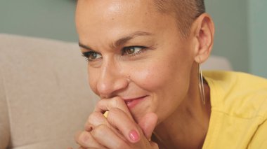 Oturma odasında kanepede yatarken dizüstü bilgisayar kullanan kel bir kadın.