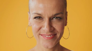 Genç mutlu, tüysüz kadının yakın plan portresi. Gözlerini açıyor. Stüdyoda sarı arka planda izole edilmiş kameraya bakıyor.