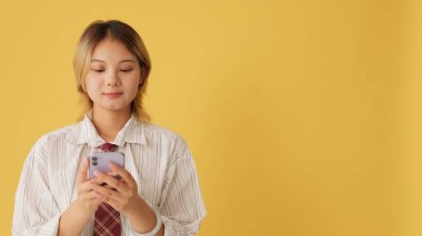 Cep telefonu kullanan genç bir kadın. Stüdyoda sarı arka planda izole edilmiş bir model alanı.