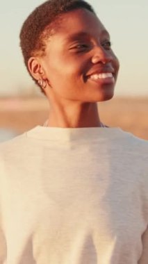 Gülümseyen genç kız güneşe bakıyor, kumsalda yaz şafağını selamlıyor.