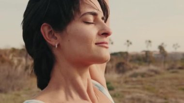 Yazın dışarıda yoga yapan gevşemiş, gülümseyen atlet kadının yakın çekim yan görüntüsü.