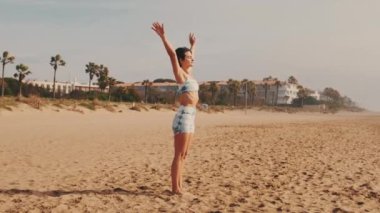 Bir kız kumsalda meditasyon yapıyor. Kumun üzerinde duruyor. Yoga dersleri ve Asana Rehberi videosu..