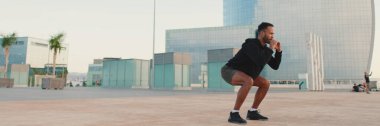 Young bearded male athlete doing workout, squats and jumping on the waterfront