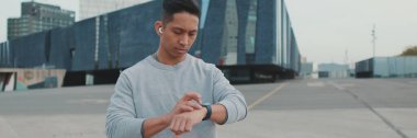 Sporcu, spor giyimli, tanınmayan genç adam akıllı saate bakıyor, panorama