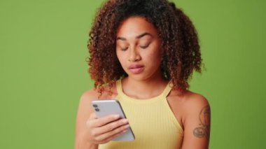 Yeşil ekranlı arka planda akıllı telefon kullanan sevimli genç bir kadın iyi bir haber alıyor.