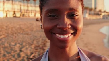 Gün doğumunda sahilde, kameraya bakıp gülümseyen çekici bir kızın portresi.