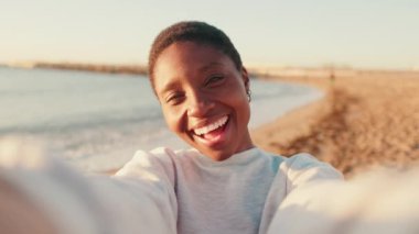 Deniz kenarında yürürken gülümseyen ve selfie çeken mutlu bir kızın portresi.