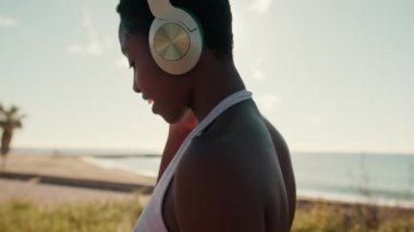 Kulaklık takan bir kızın arka görüntüsü güneşli bir yaz gününde hafifçe dans ederek sokakta yürüyor.