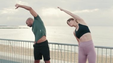 Atletik çift yan eğilip birlikte ısınıyor.