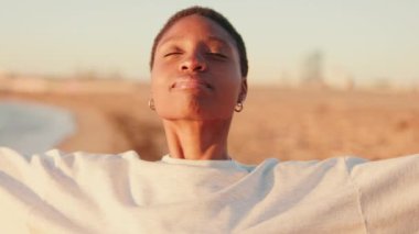 Bir kız gülüyor ve kollarını kaldırıyor şafak vakti kumsalda.