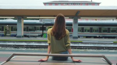 Tren istasyonunda bir bankta oturan genç bir kadın.