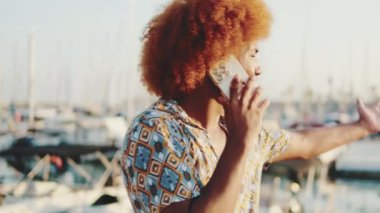 Deniz kenarında telefonla konuşan afro saçlı komik adamın yan görüntüsü. Kamera etrafında döner.