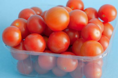 Mavi arka planda bir kutu taze vişneli domates.