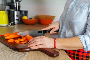 Mutfakta bıçaklı bir kadın havucu parçalara ayırıyor.