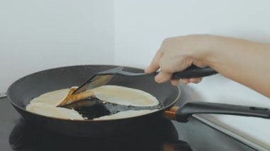 Tanınmayacak halde olan kişi tavada un keki kızartır, sadece kollar görünür.