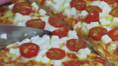 Domatesli ve peynirli pizza yakından kesiliyor, hiç kimse görünmüyor, sadece bıçak var.