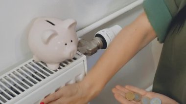 Tanımlanamayan yüzü olan biri, ısıtmak için biriktirdiği parayı kumbaraya yatırıyor, sadece bacakları ve kolları görünüyor.