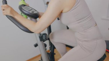 Yakından, tanınmayan yüzü olan kişi egzersiz bisikletinde egzersiz yapıyor, sadece bacakları ve kolları görünüyor.