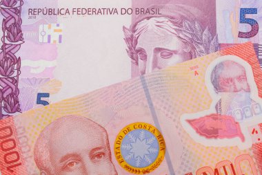 Brezilya 'dan gelen pembe ve mor beş gerçek banknotun makro görüntüsü Kosta Rika' dan gelen bin colonluk renkli bir banknotla eşleşti. Makro çekimde yakın çekim.