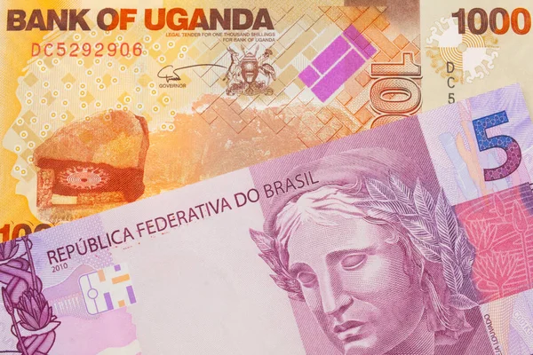 ブラジルのピンクと紫の5つの本物の銀行券のマクロ画像は ウガンダからのオレンジと白の1 000シリング紙幣と対になりました マクロでショットを閉じる — ストック写真