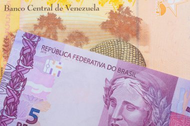 Brezilya 'dan gelen pembe ve mor beş banknotun makro görüntüsü ile Venezuela' dan gelen renkli, sarı beş Bolivar banknotu eşleşti. Makro çekimde yakın çekim.
