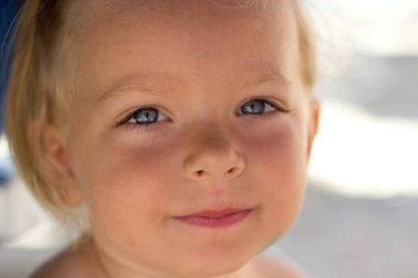 Little blond girl smiling with beach on background,positive portrait of european toddler,adorable kid on the beach,cute smiling child looking at camera.