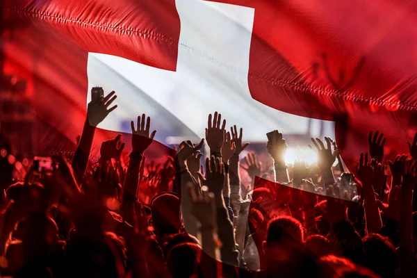 football fans supporting Switzerland - crowd celebrating in stadium with raised hands against Switzerland flag
