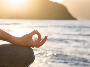 Gün batımında deniz kenarında meditasyon yapan kadın.