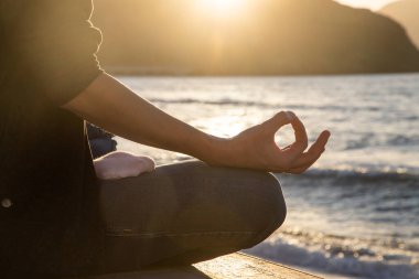 Gün batımında deniz kenarında meditasyon yapan kadın.