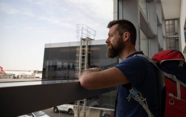 Sırt çantalı yakışıklı adam havaalanında bekliyor.