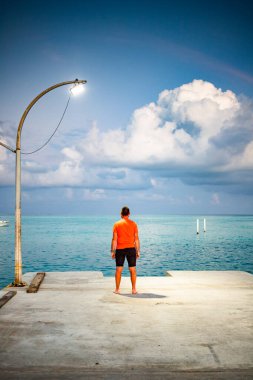 Tropikal deniz özgürlüğünün üzerindeki gün batımı bulutuna bakan adam.