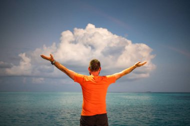 Tropikal deniz özgürlüğünün üzerindeki gün batımı bulutuna bakan adam.