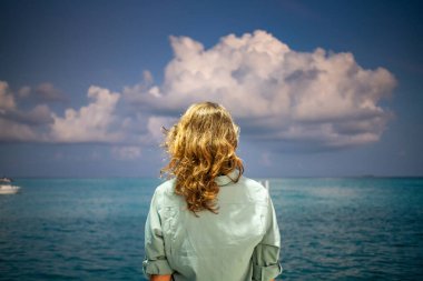 Kadın tropik deniz özgürlüğünden pembe gün batımına bakıyor.