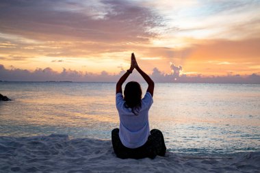 Tropik plajda gün batımında yoga yapan bir kadın.