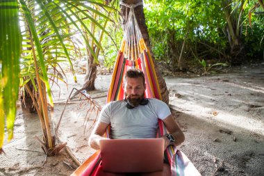 Egzotik sahilde dizüstü bilgisayarda çalışan bir adam.