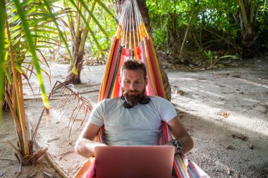 Egzotik sahilde dizüstü bilgisayarda çalışan bir adam.