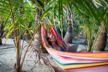 Egzotik sahilde dizüstü bilgisayarda çalışan bir kadın.