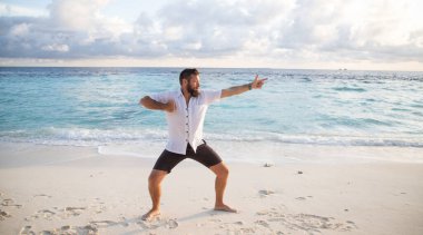 Adam deniz kenarında qigong çalışıyor.