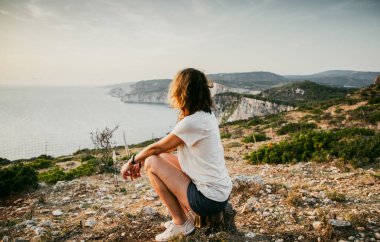 Kadın turist rahatlıyor ve denizde kayaları seyrediyor.