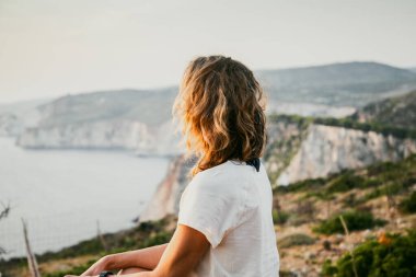 Kadın turist rahatlıyor ve denizde kayaları seyrediyor.