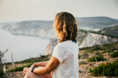 Kadın turist rahatlıyor ve denizde kayaları seyrediyor.