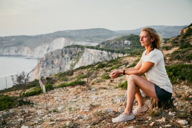 Kadın turist rahatlıyor ve denizde kayaları seyrediyor.